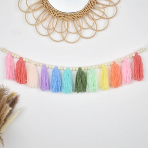 Detail of bohemian rainbow yarn tassels and natural wood beads on a white wall decor