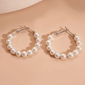 Detail of round faux pearl hoop earrings with silver-tone clasps on a beige background