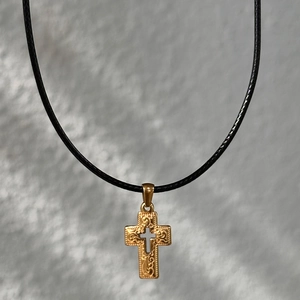 Macro shot of 18k gold-plated stainless steel cross pendant with vintage black leather cord