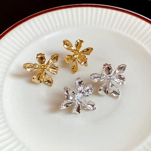 Detailed view of silver and gold metal flower stud earrings on a ceramic tray