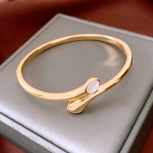 Detail of gold-plated oval bangle with white inlay on a gray jewelry box and brown silk