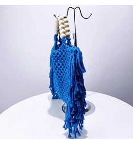 Blue woven mini handbag with tassel fringe detail and wooden bead handle on a metal rack