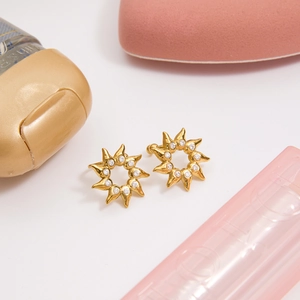 Vue macro de boucles d'oreilles soleil dorées avec strass sur fond rose poudré