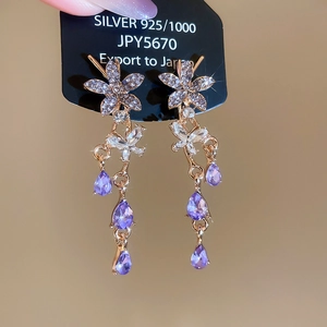 Detail of silver drop earrings with tassel, diamond flower, and purple teardrop crystals