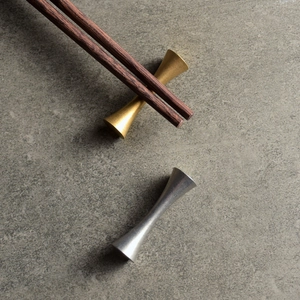 Modern gold and silver hourglass chopstick rests on a textured grey slate background