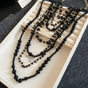 Macro detail of multi-layered acrylic black beaded tassel necklace with gold clasp