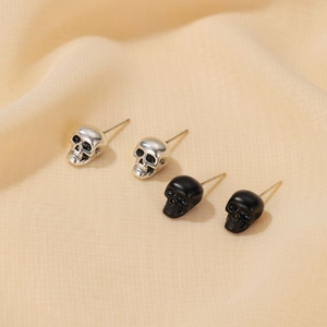 Macro shot of silver and black skull stud earrings on beige fabric background