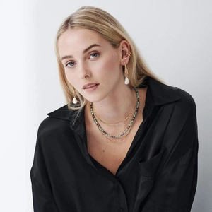 Detail of layered gold necklaces with colorful beads and pearl earrings on a model