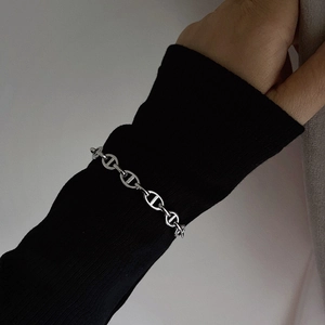 Close-up of a silver anchor chain bracelet worn over a black sweater sleeve
