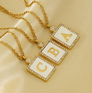 Macro view of gold square initial pendant with white enamel and sparkling zircon frame