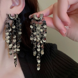 Detail view of U-shaped gunmetal earrings with long sequined tassels on a model ear