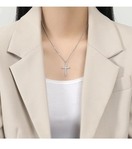 Detail of silver faith cross necklace with clear zircons worn by a model in a beige suit