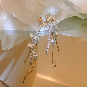Détail de boucles d'oreilles nœud avec perles, cristaux et longs glands dorés
