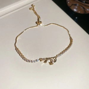 Detailed macro view of a gold bow bracelet with micro-pave zircons and adjustable bead closure