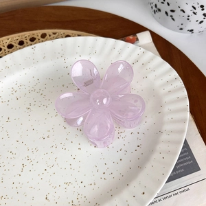 Detailed close-up of a purple translucent flower hair claw clip on a ceramic tray