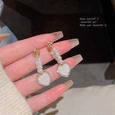 Detailed close-up of gold plated heart earrings with white mother of pearl and pearls
