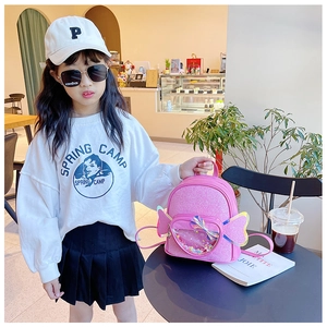 Girl wearing pink sequin wing backpack with white sweatshirt and pleated black skirt