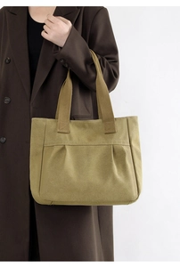 Detailed side view of a large olive green canvas tote bag worn by a model in soft light