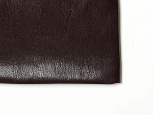 Dettaglio macro della texture in pelle marrone scuro su cintura e gonna coordinata