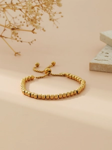 Macro detail of gold beaded bracelet featuring textured faceted beads and adjustable slider