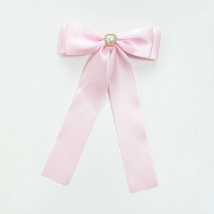 Détail d'un nœud en satin rose avec perle en cœur et broderie dorée sur l'accessoire
