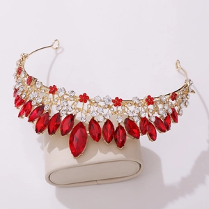 Close-up of golden bridal tiara with red marquise gems and white crystals on a beige stand