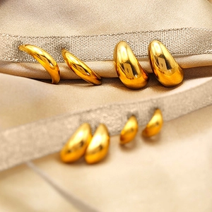 Macro shot of gold teardrop earrings resting on luxurious champagne silk fabric