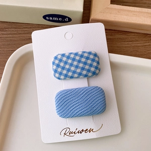 Close-up of blue plaid and textured fabric hair clips set on a white display card