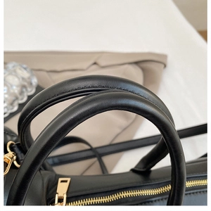Detail of black leather handbag featuring round handles and polished gold hardware