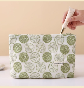 Detail of embroidered canvas makeup bag with green leaf pattern and zipper closure