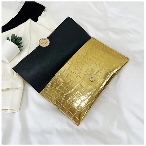 Macro view of golden crocodile embossed clutch with round magnetic snap and black lining