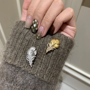 Macro detail of gold and silver feather brooches with rhinestones on a brown knit cuff