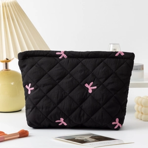Detailed close-up of a black quilted makeup bag with pink bow embroidery on a vanity
