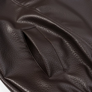Detailed macro view of dark brown litchi textured faux leather jacket pocket with double stitching