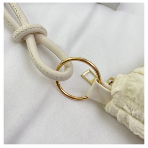 Dettaglio della tracolla in pelle beige annodata e anello in metallo dorato su borsa a pieghe