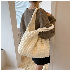 Side view of beige bubble puff shoulder bag worn by model in minimalist room