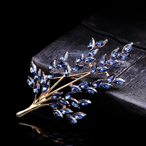 Elegant gold wheat brooch with blue crystals on a dark reflective luxury background