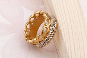 Close-up of golden infinity ring with triple-row pavé crystals on a wooden background