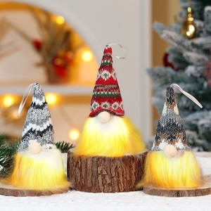 Three glowing Christmas gnomes with knitted hats and warm LED lights on wood