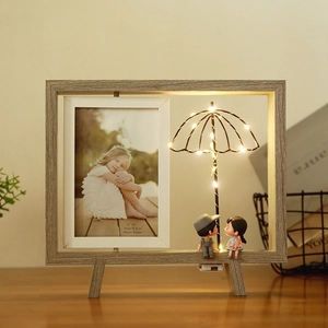 Détail d'un cadre photo rotatif en bois avec éclairage LED et figurines de couple
