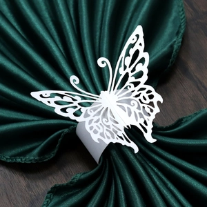 Detail of laser-cut white butterfly paper napkin ring on a dark green satin cloth
