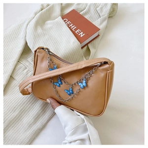 Close-up of khaki shoulder bag with silver chain and blue butterfly pendant detail
