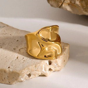 Macro shot of 18k gold irregular liquid metal ring on a rustic beige stone pedestal
