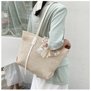 Detail of a beige straw tote bag featuring delicate pink floral lace trim and white leather straps