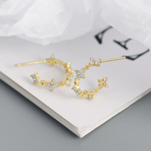 Close-up of C-shaped gold earrings featuring four-leaf clover motifs and blue opal stones