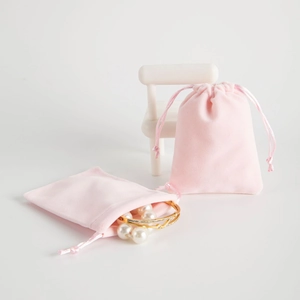 Pink velvet drawstring jewelry pouch with pearl bracelet on decorative mini furniture