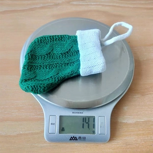 Detailed close-up of a green knitted Christmas stocking ornament weighing 14.1g on a scale