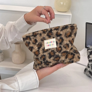 Close-up of leopard print plush makeup bag featuring a logo patch and top zipper detail