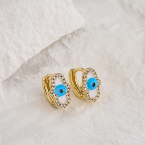 18K gold plated Hamsa hand earrings with blue evil eye zircon on white stone background