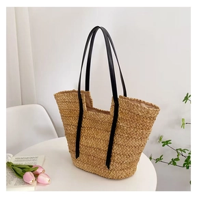 Détail d'un grand sac cabas en paille avec anses noires sur une table blanche